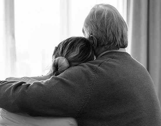 Una pereja de espaldas, abrazados miran la luz que entra por una ventana, através de las cortinas.