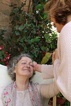 Mujer en sus últimas horas de vida, sentada, mientras recibe una cariñosa caricia en la cara, por parte de un ser querido.
